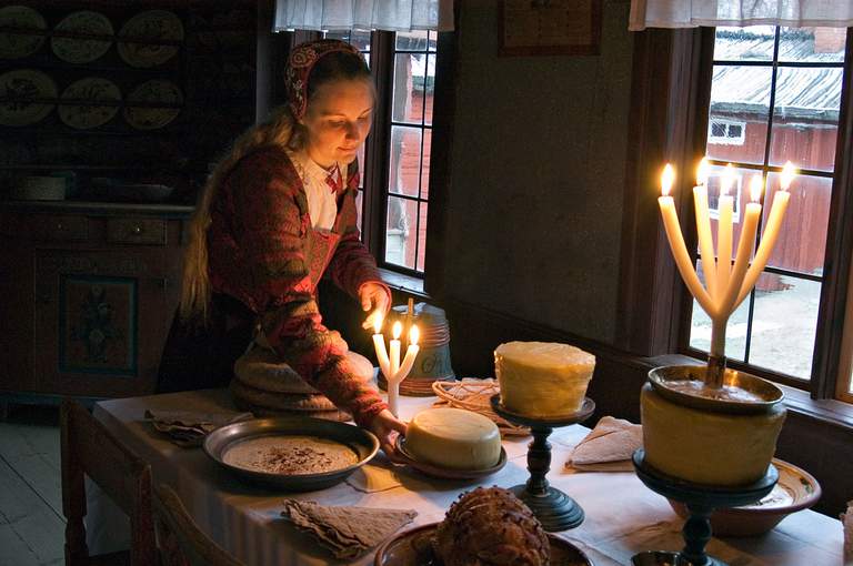 A woman in traditional clothes at a table with dishes and candles.