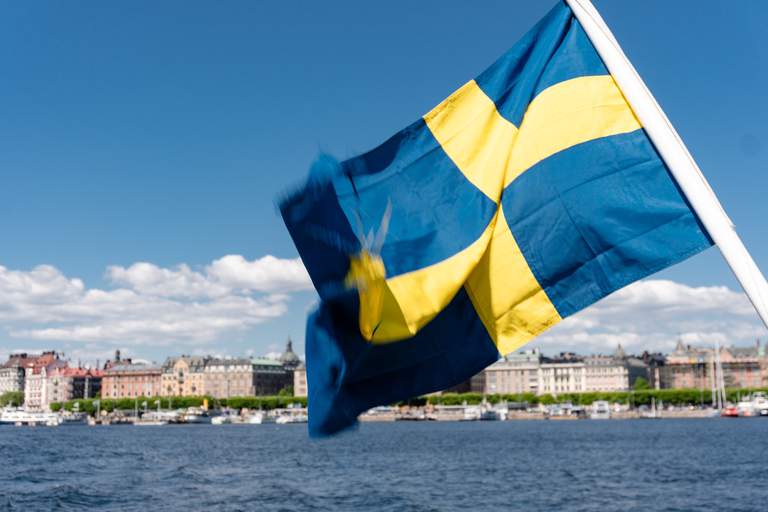 Summer in Stockholm. A blue and yellow Swedish flag is swaying in the wind. Behind it in the distance is central Stockholm.