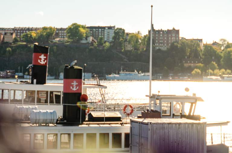Sommar i Stockholm. Två Strömmafärjor ligger vid kajen vid Stadshuset. På andra sidan vattnet syns Södermälarstrand.