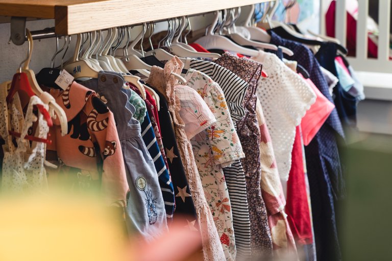 Children’s clothing on hangers in a shop, with colorful garments and a variety of patterns and fabrics.