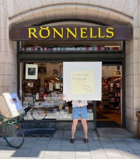 A person stands outside the Rönnells bookstore holding up a large record cover.