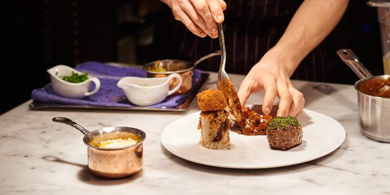 A pair of hands are preparing food to be served for dinner at restaurant Luzette. The lights are dim and the person is making the last finishing touches to the dish.