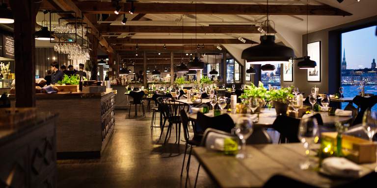 The beautiful space of Fotografiskas restaurant looks almost like an attic or a loft with large visible beams. Large windows show an evening view over Stockholm.