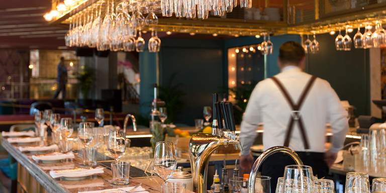 The bar at Haymarket is set for dinner with cutlery and glasses in front of each bar stool. Glasses hang above the bar in the usual style of an urban bar in the city.