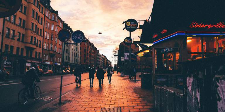 Höst, solnedgång över Hornsgatan. Folk passerar kameran till fots och på cykel. Hornsgatan är en av stadsdelens mest trafikerade och sträcker sig från Södermalmstorg i öst till Hornstull i väst. Sträckan däremellan kantas av några av Söders populäraste barer och nattklubbar, unika butiker, mysiga kaféer och historiska byggnader.