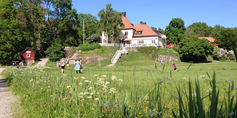 Summer in the Stockholm Archipelago. Pictured is a family playing on a green meadow. A residential two-story villa is visible in the background. The picture was taken on the island of Grinda.