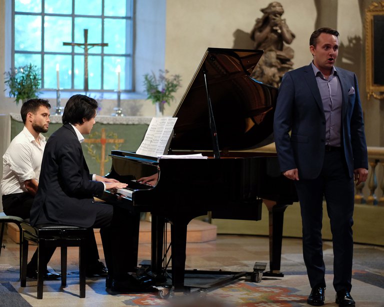 A pianist playing the grand piano and a singer standing and singing.