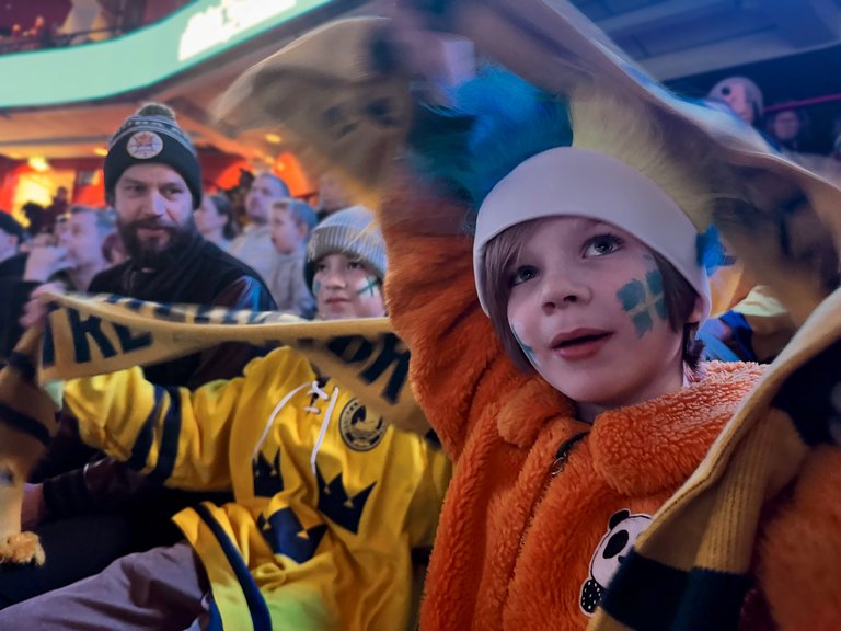 Hockey fans in team gear watching a game from the stands.