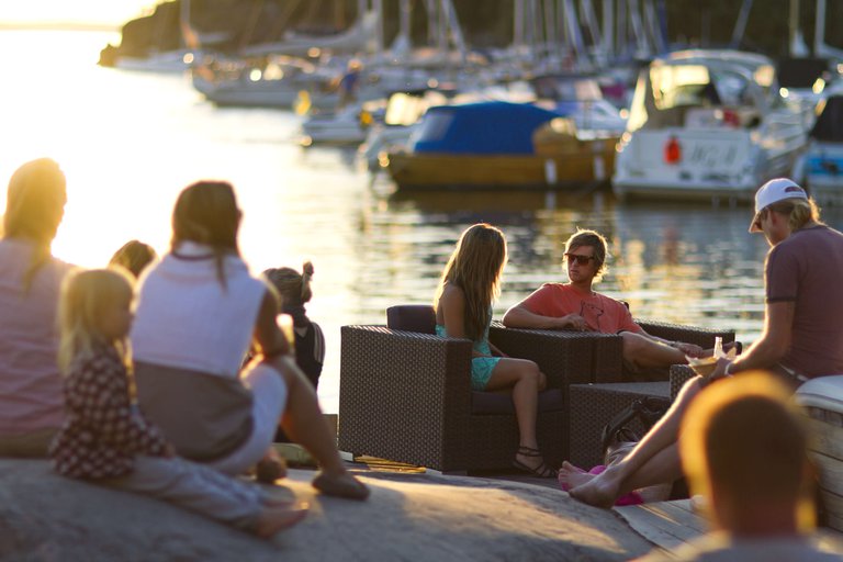 A group of people sit outdoors in the summer at sundown on the island of Grinda in Stockholm's archipelago.