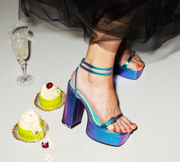 Feet in high-heeled shoes, two cakes and a wine glass on the floor.