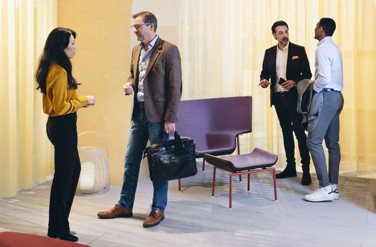 Four people stand talking in a meeting room.