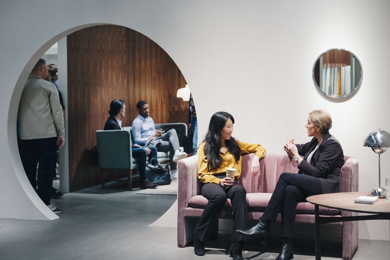 Casual business meetings in Stockholm. Two women sit chatting on a couch in the foreground, while two men sit and talk on a couch in the background.