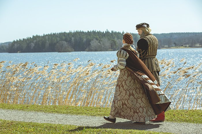 Two people in historic costumes walking on a shore of a lake.