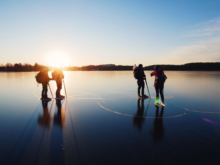 4 people ice skating on a frozen late on a sunny winter day