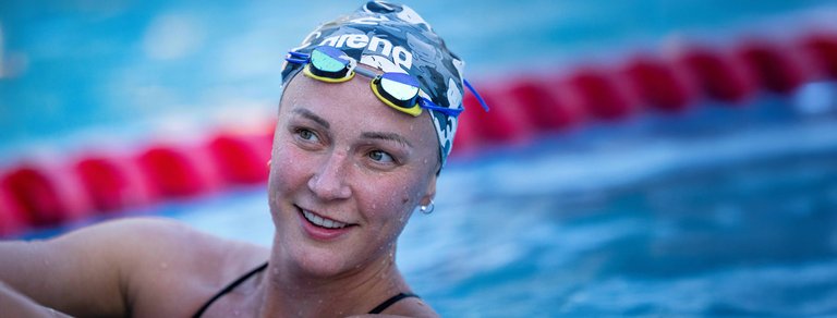 Sarah Sjöström smiling in a swimming pool, wearing a swimsuit and swim cap.