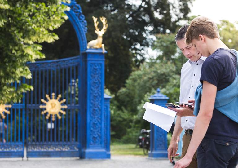 Two persons looking at their mobile phones near The Blue Gate at the entrance to Djurgården.