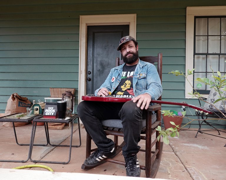 The musician Lee Bains is sitting in a chair with his guitar on his knees.