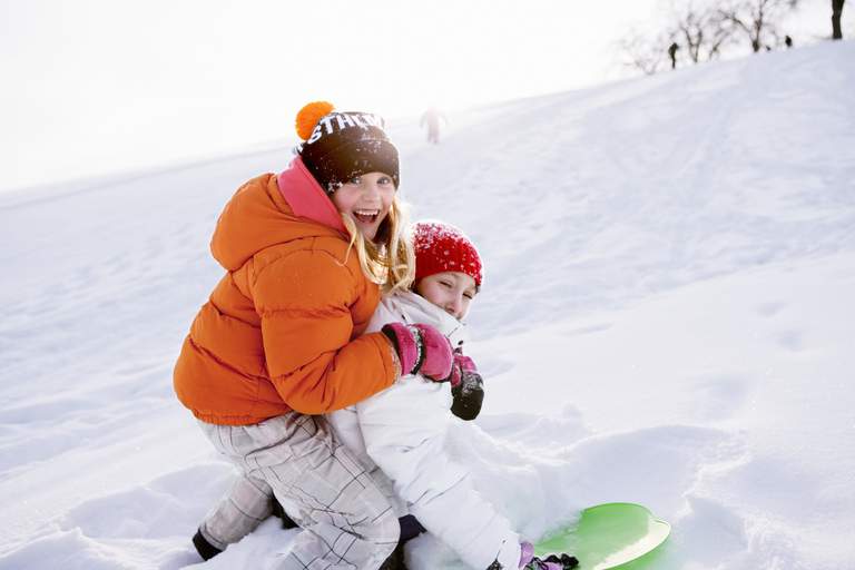 Two kids sledding down a snowy hill in Stockholm