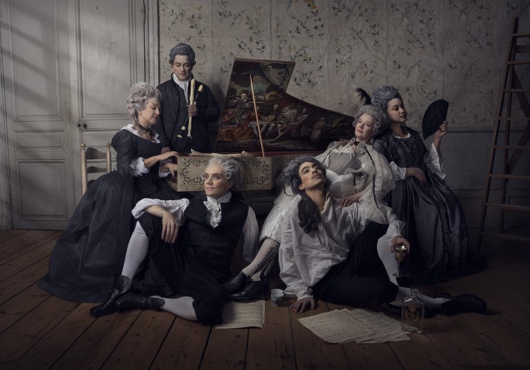 Musicians in historical costumes sitting beside a grand piano
