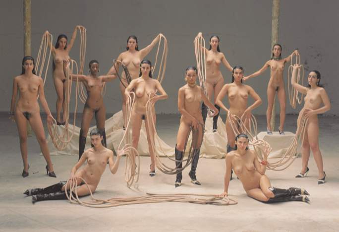 A group of naked women stare into the camera without smiling. They all look assertive and they are all joined by freakishly long fingernails (or ropes) between their outstretched hands.