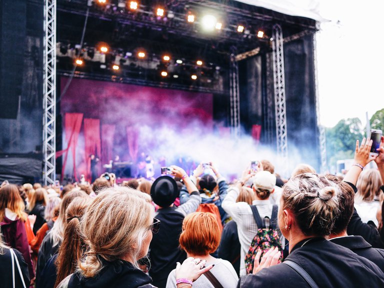 A crowd in front of a large stage, with colorful lighting and smoke