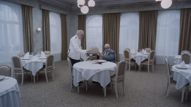 A person sitting at a table in a restaurant and a waiter serving him wine.