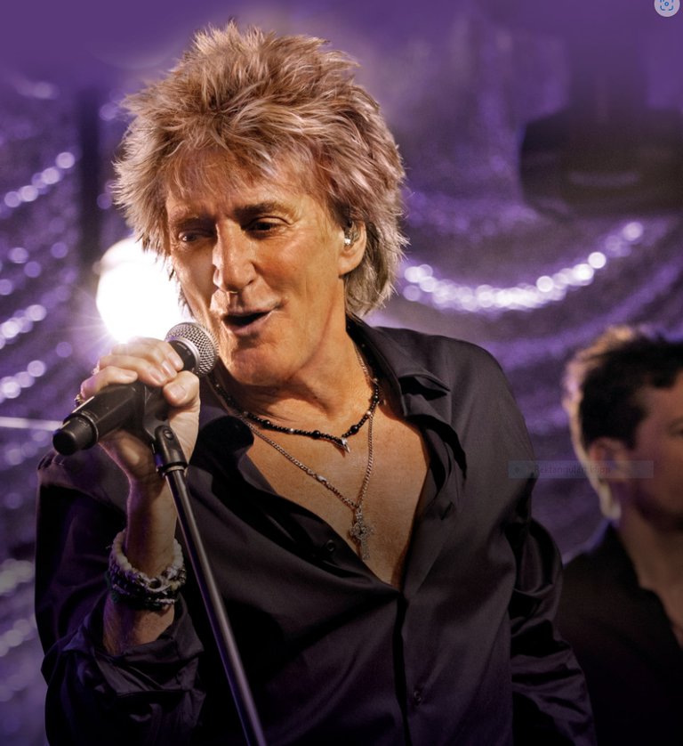 Rod Stewart is holding a microphone and singing.
