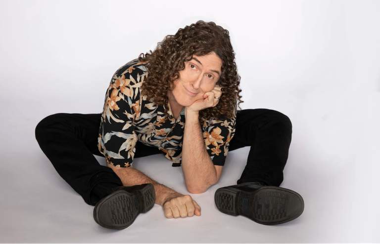 The artist “Weird Al” Yankovic sitting on the floor.