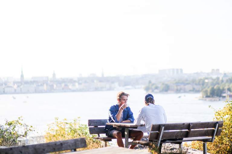 Two men enjoy a coffee break outdoors at a picnic table on Södermalm in Stockholm.