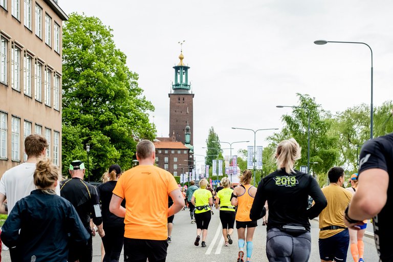 A group of people photographed from behind running on a Stockholm street with the City Hall as a backdrop