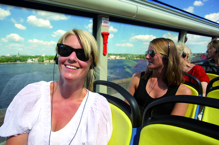 Tourists onboard Hop-On Hop-off bus listening to an audio-guided tour.