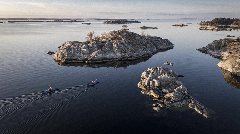 Two kayakers glide through calm waters between rugged, tree-topped islands under a soft evening sky.