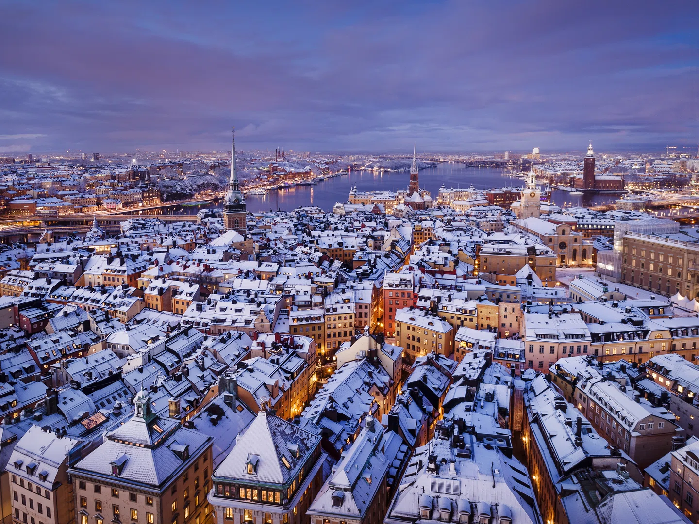 View of Stockholm in winter, showing snow covered buildings and light cloud in the sky. Early evening lights reflecting off the water. From https://www.visitstockholm.com/