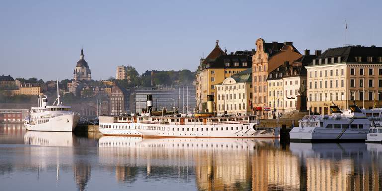 A view over the historical buildings by the water front at Gamla Stan in Stockholm. Boats and ships have docked and line the harbour.