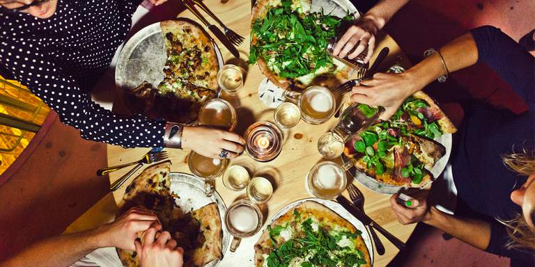 A group of people are sharing a few pizzas at Bistro Bananas, the food is as trendy as the minimalist table settings and decorated with fresh herbs.