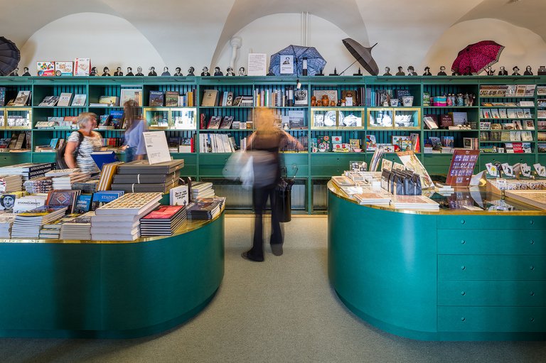 Muser i Stockholm. Museumbutiken på Stadsmuseet. Böcker och diverse souvenierer står på butikens gröna hyllor. Några museibesökare syns på bilden, i rörelseoskärpa.