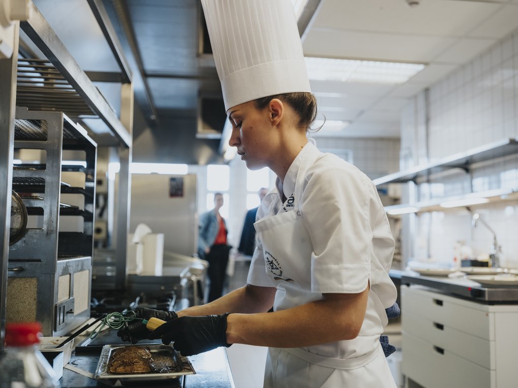 Chef in a professional kitchen checking the temperature of meat on a tray.