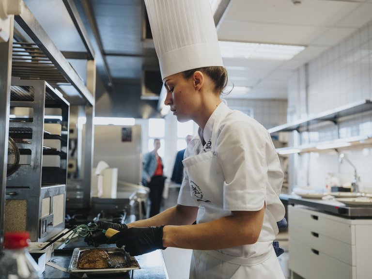 Chef in a professional kitchen checking the temperature of meat on a tray.