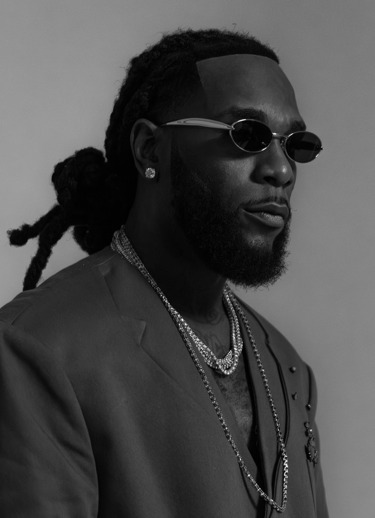 A man wearing a suit jacket, sunglasses and various pieces of jewlery.