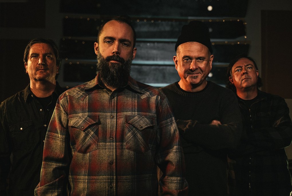 Four middle-aged men standing in a dimly lit room.