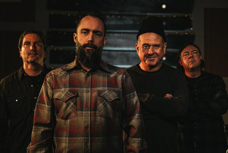 Four middle-aged men standing in a dimly lit room.