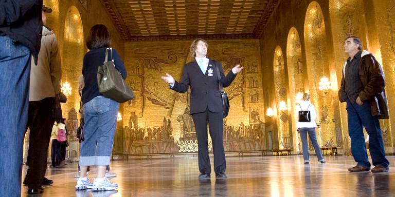 A guide takes a small group of tourists through Gyllene salen (The Golden Hall) in Stockholm City hall. A relief of St. Erik, Stockholm’s patron saint, can be seen on the far wall behind the tour guide. Visit Stockholm is tasked with authorizing guides. The guides are all trained and certified, and together they speak 30 different languages, including sign language.