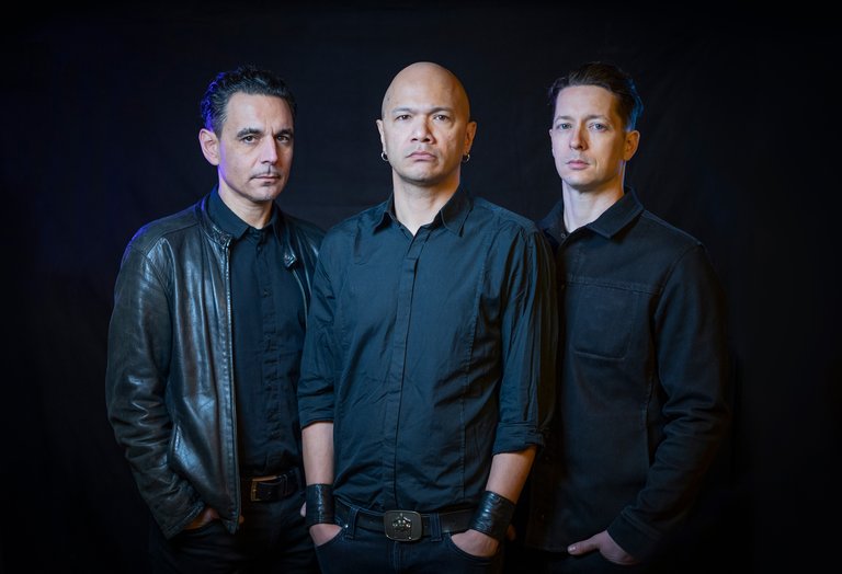 Three men in black shirts against a black backdrop.
