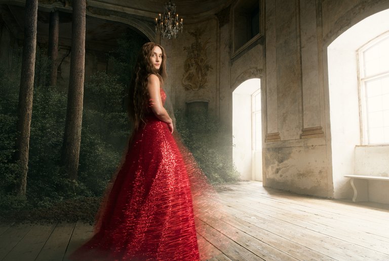 A woman in a red dress standing in a room in a castle that's in the process of turning into a forest.