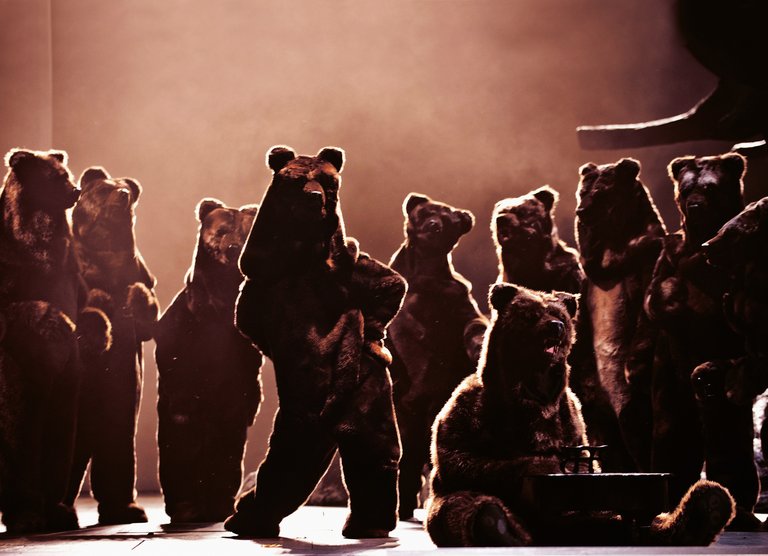 A dozen actors in bear costumes on a stage.