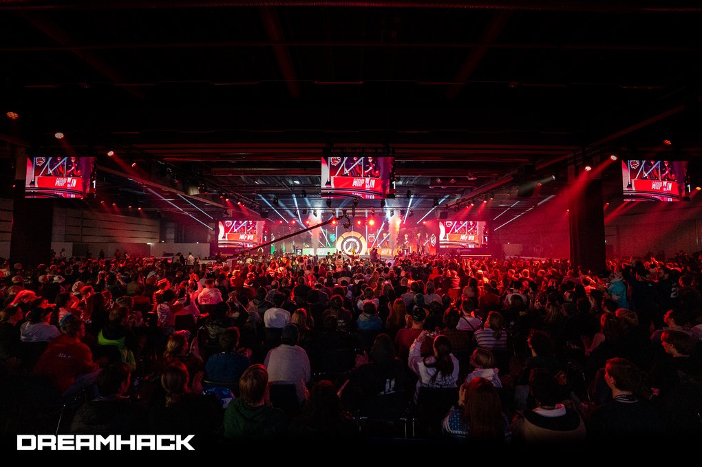 A sea of people in front of a brightly lit stage in a huge, dimly lit hall.