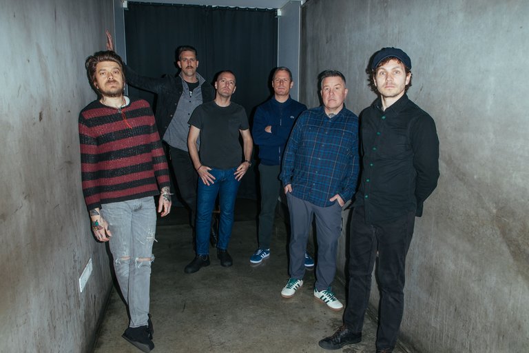Six casually-dressed men standing in a concrete corridor.