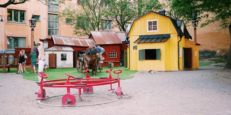 A children’s carousel in the foreground, small historical looking playhouses in bright colours in various sizes are visible behind it.