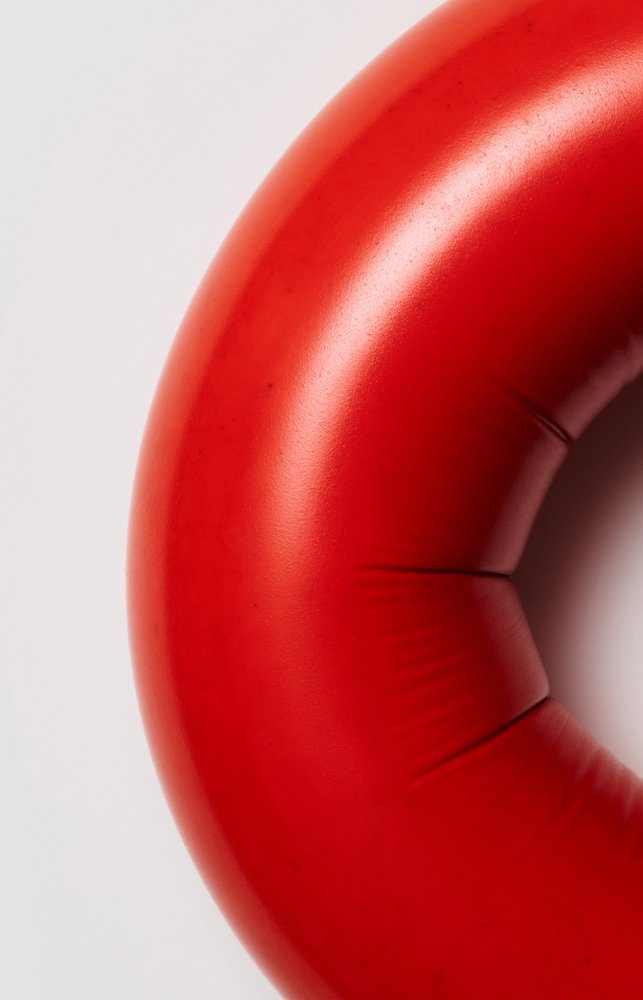 A red, glossy ring with creases and seams fills most of the image. It is a large sausage, photographed close up.