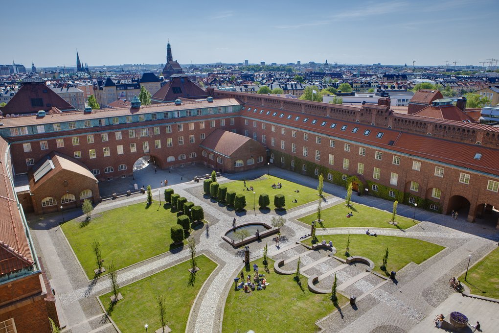 Aerial view of KTH’s courtyard with red-brick buildings, green lawns, and people relaxing in the sun.